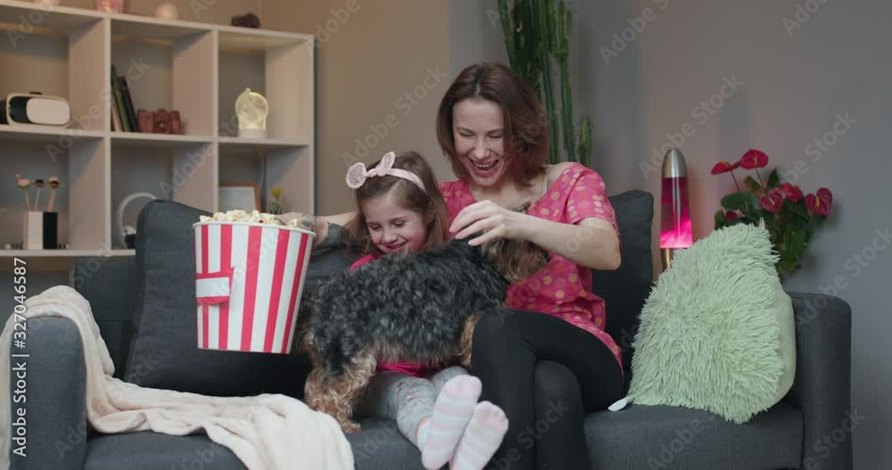 Happy family living room and sitting down on sofa to watch TV. Cute little dog following them and wagging its tail