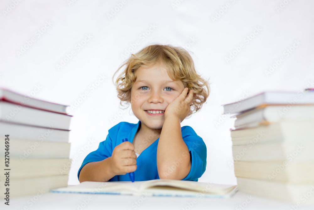 Little happy child between 4 and 5 years old sitting at a desk studying while holding a pencil with textbooks on his table Little happy child between 4 and 5 years old sitting at a desk studying while holding a pencil with textbooks on his table