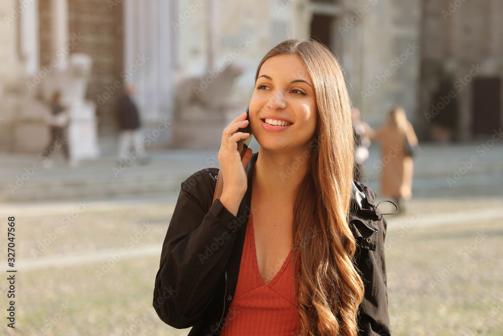 Happy young smiling woman talking on mobile phone on European city street. Lifestyle portrait.