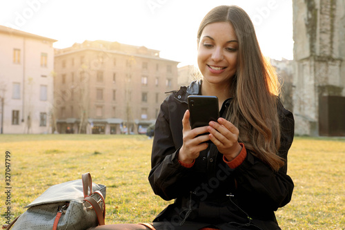 Student girl sitting on grass messaging with mobile phone outdoor on spring time photo