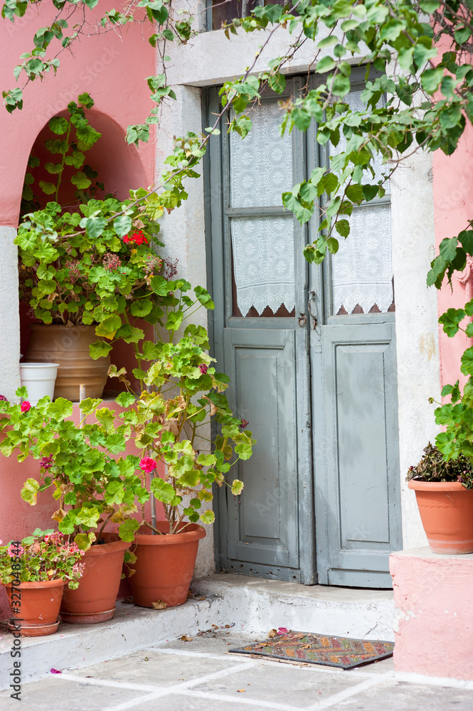 Empty view of quaint Mediterranean doorway with pink stucco walls framed by potted geranium plants and vines
