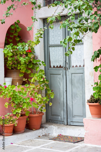 Empty view of quaint Mediterranean doorway with pink stucco walls framed by potted geranium plants and vines © PeskyMonkey