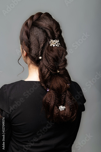 Weave, braid tail hairstyle. Hairstyle on brown hair woman with long hair on a gray background. Professional hairdressing services.Hair styling, making braid with hairpin.