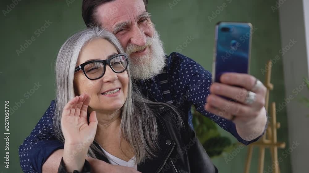 Good-looking happy smiling senior man and woman having video call and woman waving hand to say 