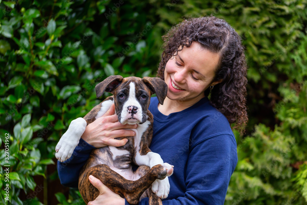 Obraz premium White Caucasian Woman with a small cute Boxer Puppy outside in the garden. Taken in Vancouver, British Columbia, Canada.