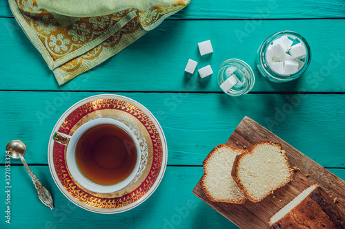 A tiffany color wooden table with a sliced cake on the cutting board, sugar cubes and two porcelain cups of tea. 