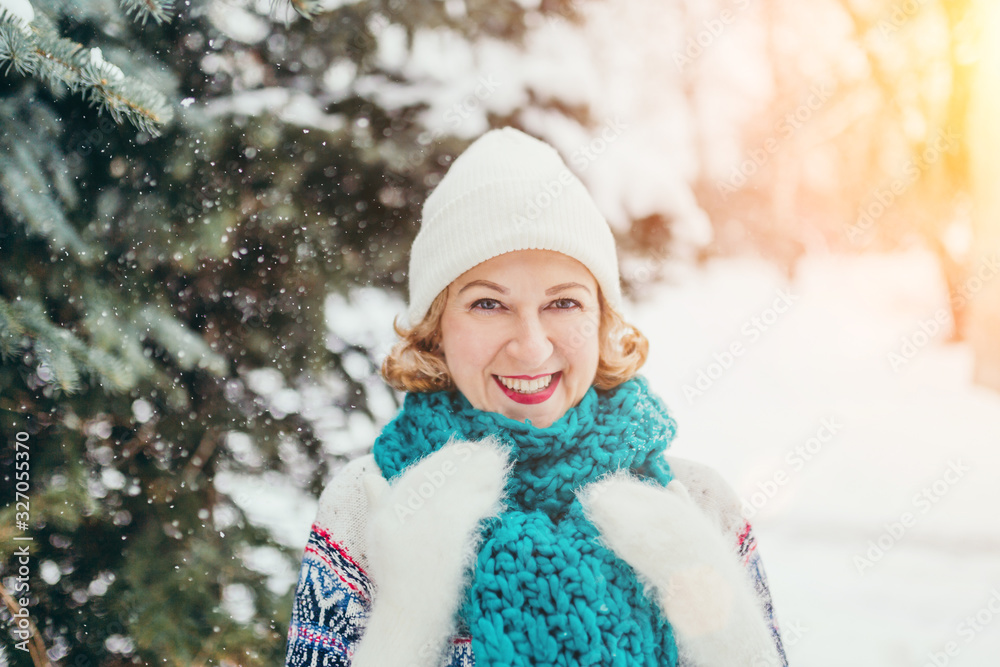 Attractive young blonde laughing closing from falling snow in the winter forest - cozy warm clothes Attractive young blonde laughing closing from falling snow in the winter forest - cozy warm clothes