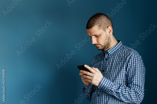 Caucasian man wearing shirt standing in front of the blue background wall using smart phone mobile to send messages sms texting or browsing internet front view © Miljan Živković