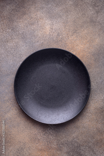 Empty black plate on brown concrete background. Top view, with copy space