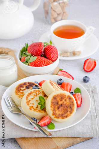 Fried cottage cheese pancakes or syrniki with fresh berries on a white plate with sour cream. Gluten free. Traditional breakfast of Ukrainian and Russian cuisine. Vertical