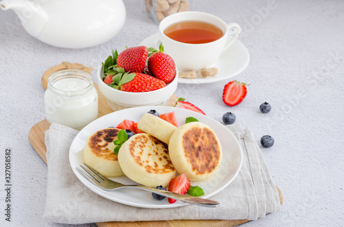 Fried cottage cheese pancakes or syrniki with fresh berries on a white plate with sour cream. Gluten free. Traditional breakfast of Ukrainian and Russian cuisine. Horizontal.