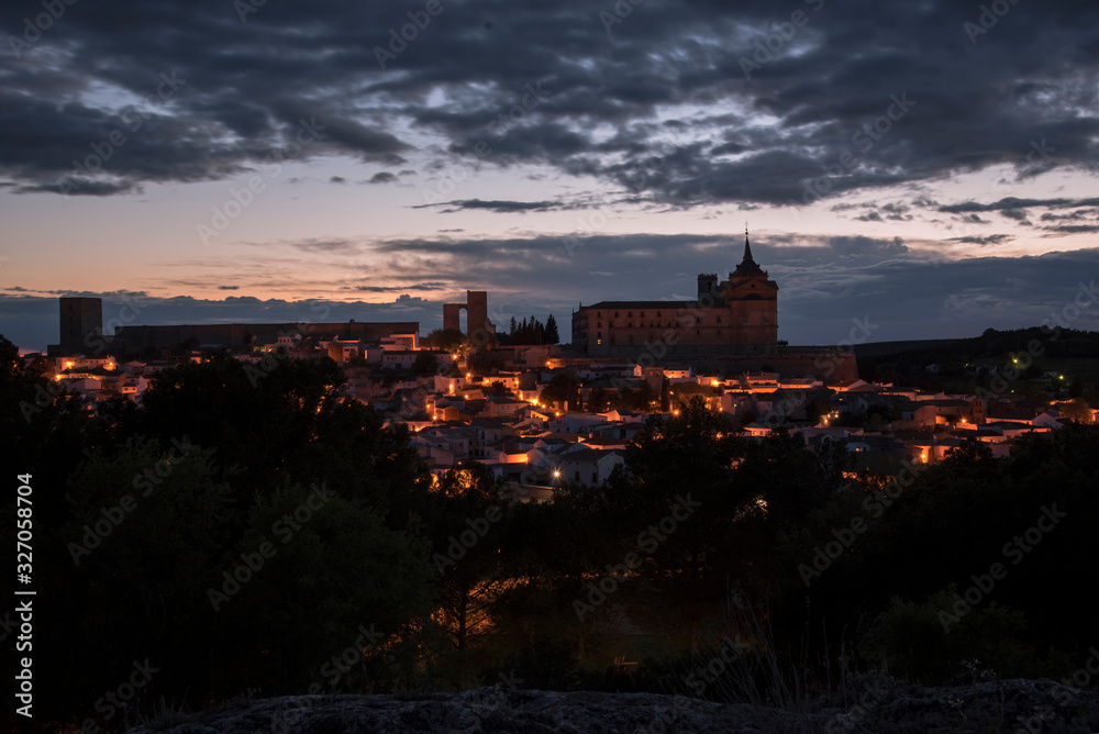 Cityscape of the illuminated town of Uclés with the monastery and castle on top of the hill at sunset, Cuenca, Castilla La Mancha, Spain