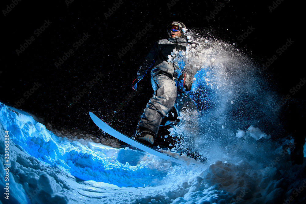 Male snowboarder doing stunts on blue light background
