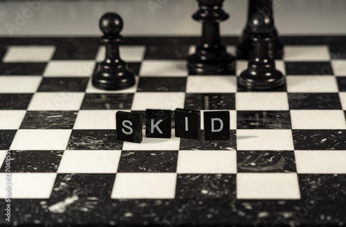 Skid (script kid) the word or concept represented by black and white letter tiles on a marble chessboard with chess pieces photo