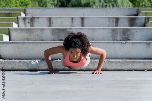 Afroamerican woman doing pushups outside on an urban park.