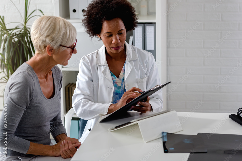 Φωτογραφία A female doctor sits at her desk and chats to an elderly female patient while lo