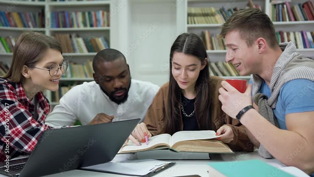 Beautiful two smiling girls and two handsome multiracial guys which together reading book while prepare for exams in the university library Beautiful two smiling girls and two handsome multiracial guys which together reading book while prepare for exams in the university library