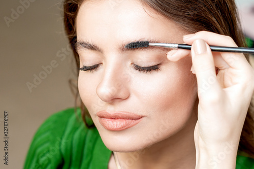 Closeup beautiful woman with eyebrow brush tool  makeup artist combs eyebrows close up.