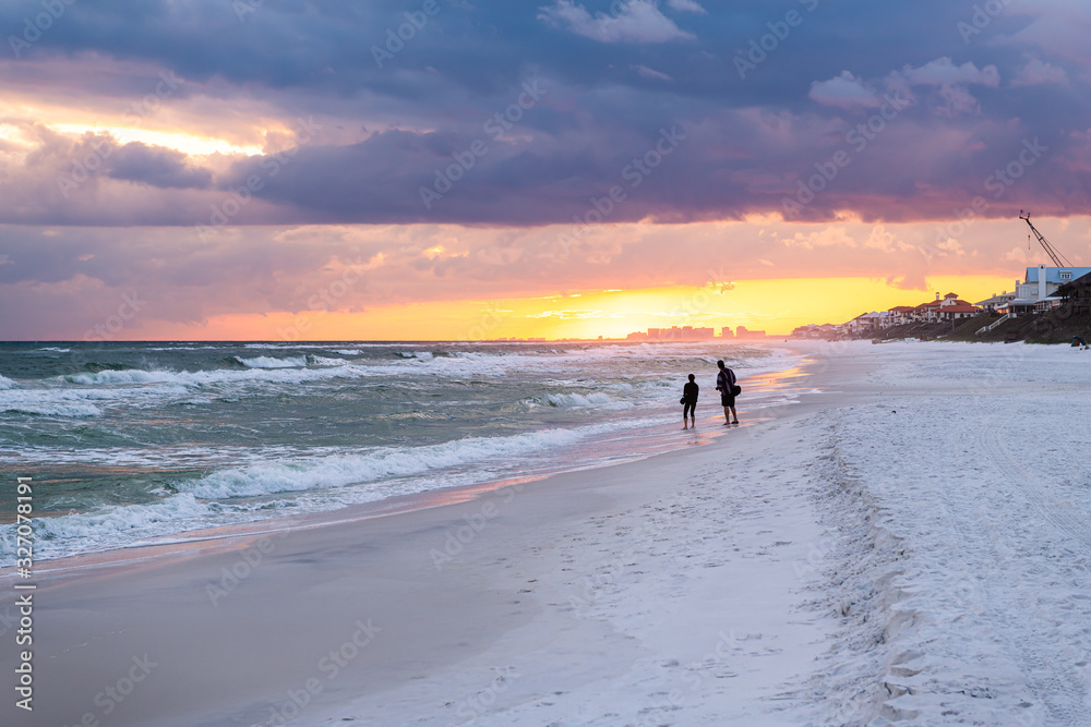 Naklejka premium Colorful pastel sunset in Santa Rosa Beach with Pensacola coast in Florida Panhandle at Gulf of Mexico ocean waves with silhouette of people