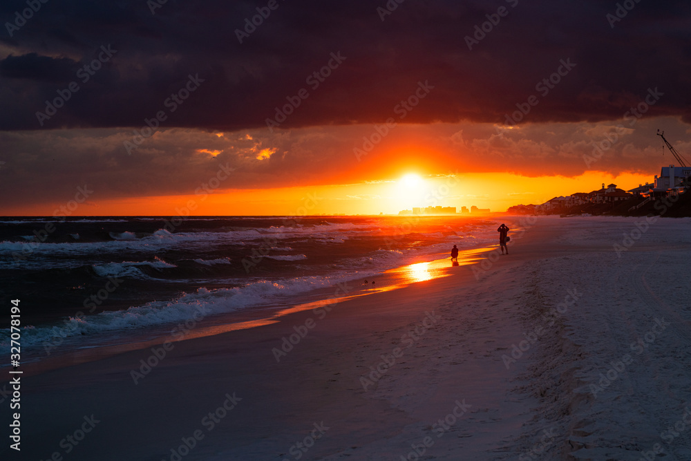 Colorful dark red sunset in Santa Rosa Beach with Pensacola coast in Florida Panhandle at Gulf of Mexico ocean waves with silhouette of people