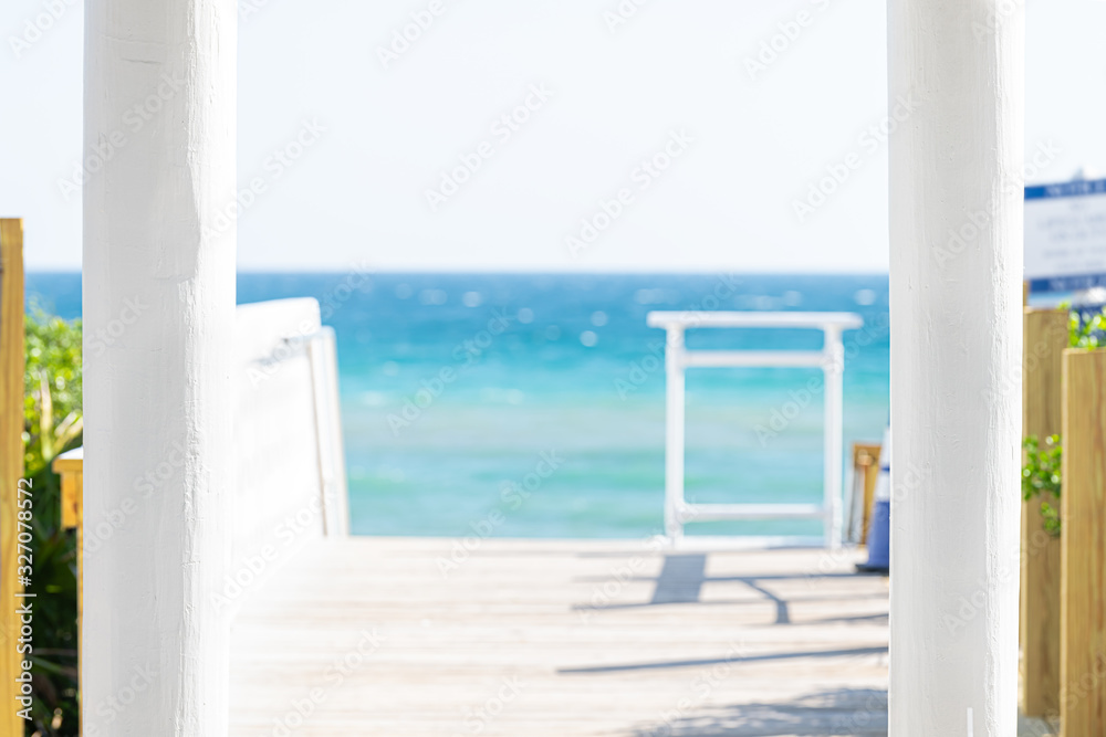 Seaside white columns in foreground with wooden boardwalk and pavilion by ocean with water gazebo in Florida architecture view during sunny day