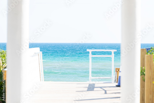Seaside white columns wooden boardwalk and pavilion by ocean with water gazebo in Florida architecture view during sunny day steps to beach