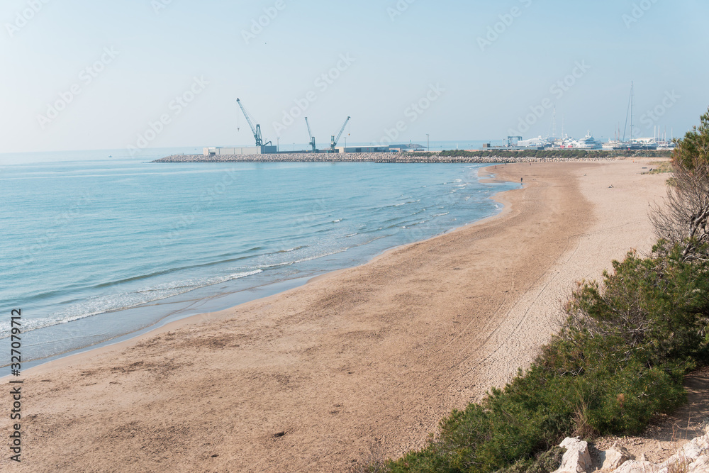 Playa de aguas azules con puerto y grúas al fondo