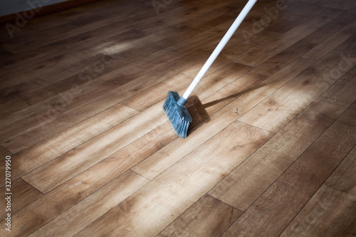 A broom consecrated by the sun rays sweeps dust from a wooden floor, parquet.