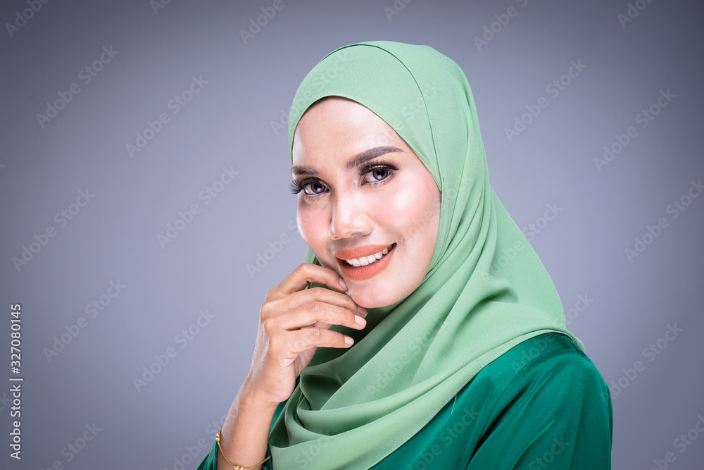 Headshot portrait of a beautiful female Muslim model in modern kurung and hijab, an urban lifestyle apparel for Muslim women isolated on grey background. Beauty and hijab fashion concept. Headshot portrait of a beautiful female Muslim model in modern kurung and hijab, an urban lifestyle apparel for Muslim women isolated on grey background. Beauty and hijab fashion concept.