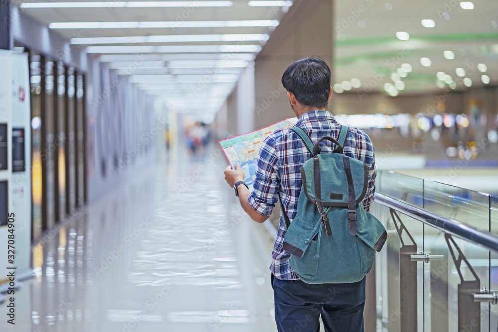 Obraz premium Asian man tourist hipster backpack to travel open map in an international airport looking at the flight information board, holding smartphone in his hand, checking flight lifestyle, Traveler concept