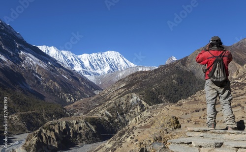 Local Nepal Man admiring landscape views of Distant Snowcapped Peaks on Annapurna Circuit Hiking and Trekking Trail in Himalaya Mountains photo