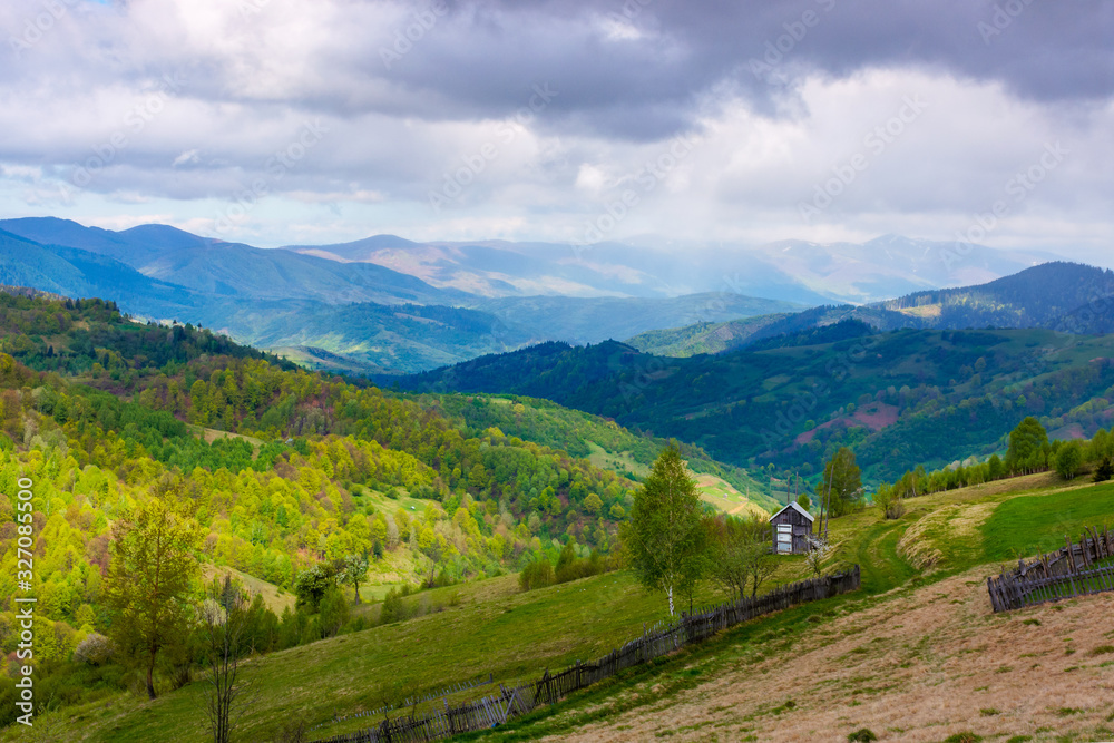 rural landscape in mountains. dappeled light on forested hills. wooden fence along the hillside. beautiful nature scenery in spring. wonderful weather with clouds