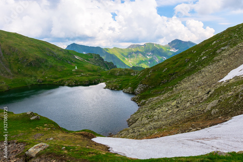 Fototapeta Naklejka Na Ścianę i Meble -  goat lake in the fagaras mountains of romania. popular travel destination. summer nature scenery with green grass and snow. ridge in the far distance beneath a cloudy sky