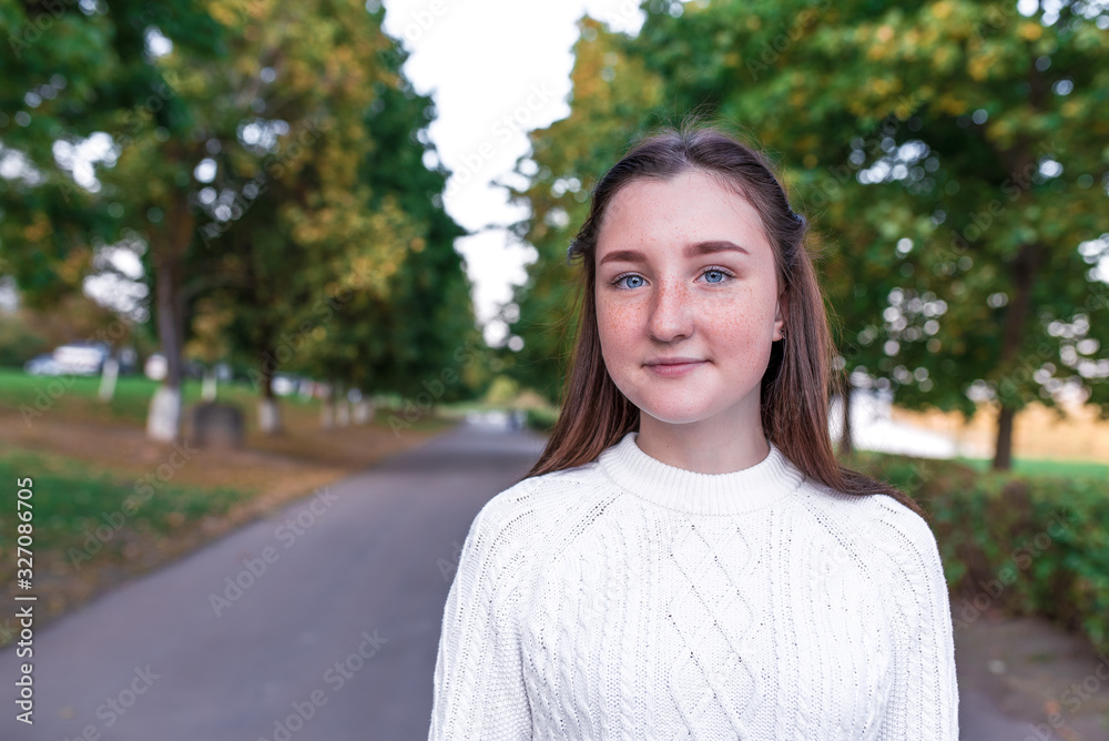 Portrait of teenage girl, summer in park, casual wear, white knitted sweater, free space for copy text. Weekend break. Freckles on face. Emotions of happiness are smiles and positive. Portrait of teenage girl, summer in park, casual wear, white knitted sweater, free space for copy text. Weekend break. Freckles on face. Emotions of happiness are smiles and positive.
