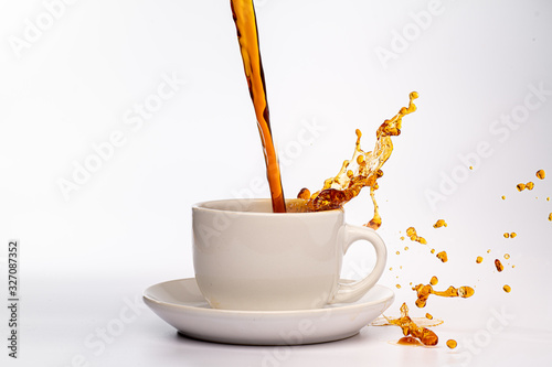 Coffee pouring into a white cup isolated against a plain white background, splashing in all directions creating a mess