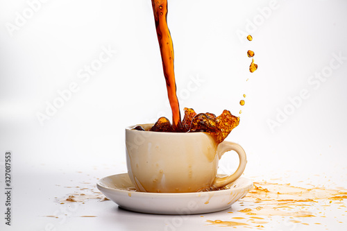 Coffee pouring into a white cup isolated against a plain white background, splashing in all directions creating a mess