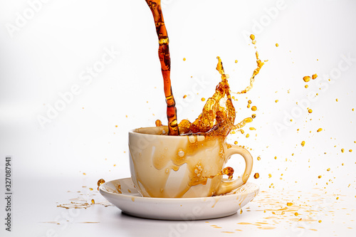 Coffee pouring into a white cup isolated against a plain white background, splashing in all directions creating a mess