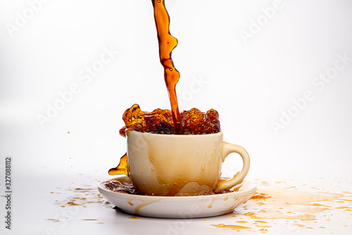 Coffee pouring into a white cup isolated against a plain white background, splashing in all directions creating a mess