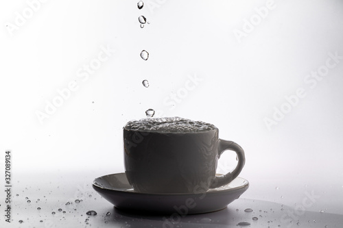 High speed studio photograph of water pouring and splashing into a white mug, isolated against a plain white background