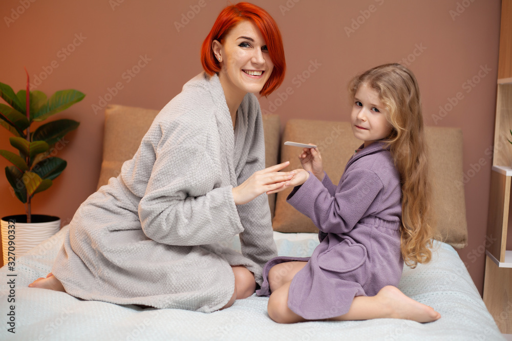 Daughter makes mom manicure at home on bed