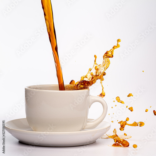 Coffee pouring into a white cup isolated against a plain white background, splashing in all directions creating a mess