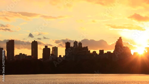 Sky, Clouds and Central Park Reservoir glow and illuminate by sunset. Central Park West Residences become silhouettes. Image was captured from Central park.