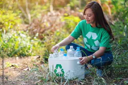 A beautiful asian woman collecting garbage plastic bottles into a recycle bin in the outdoors
