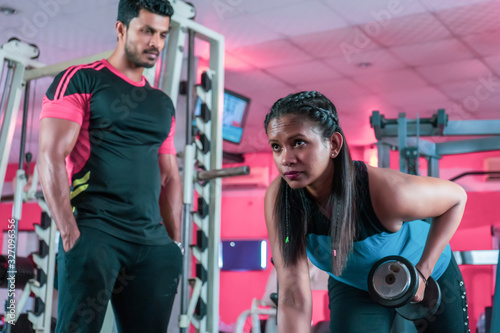 Young beautiful woman doing exercises with personal trainer and sporty girl with dumbbell