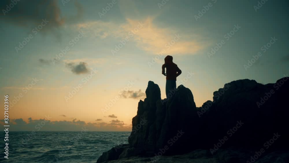 A man in a jacket stands on a rock by the sea in a stormy weather at dawn A man in a jacket stands on a rock by the sea in a stormy weather at dawn