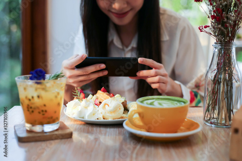 Asia beautiful woman taking photo on her waffles in the coffee shop and prepared to upload to a social app.