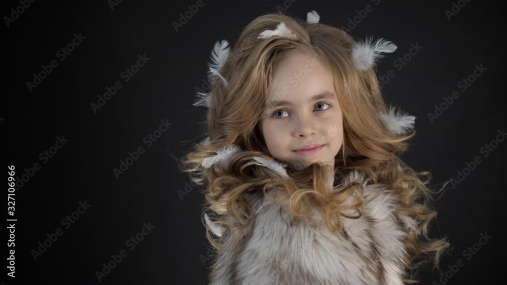 Smiling little girl looks camera in studio, beautiful fashionable cute kid model in stylish glamour clothes with curly hair on black background, preschool child with pretty face posing, lady lifestyle