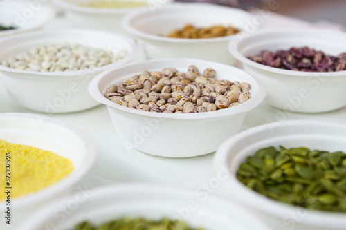 Peeled beans in a white plastic plate. Around in the same plates are various seeds, nuts and beans.