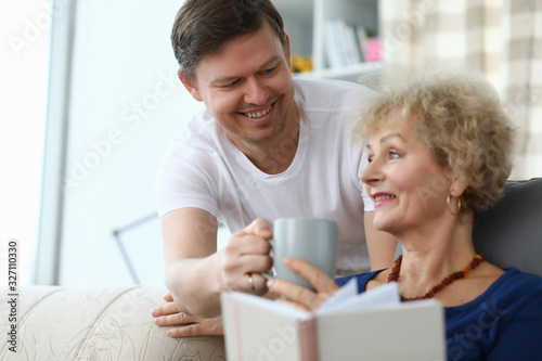 Happy son brought cup tea for an elderly mother. Son cares for an elderly mother at home. An adult son decided to stay with his mother alone. Have fun with your parents. Good family relationships