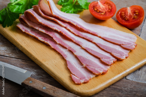 Raw sliced bacon on wooden board.